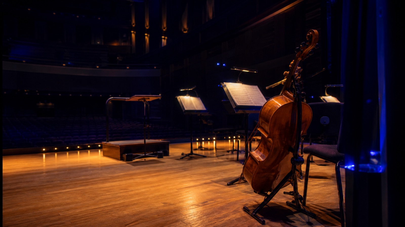 A cello waits on a dark concert stage.